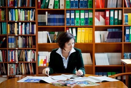 Agnieszka Grzelak podczas lektury, sfotografowana na tle biblioteczki