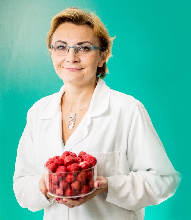 Dr Eng. Agnieszka Ciurzyńska portrait photo on a green background. In her hands she holds a glass dish filled with strawberries.