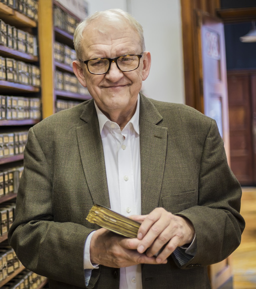 Prof. Juliusza Gardawskiego - zdjęcie portretowe na tle katalogu bibliotecznego. W rękach profesor trzyma zamkniętą książkę.