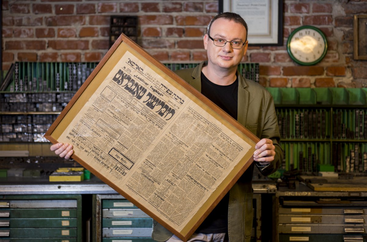 Dr hab. Adam Kopciowski prezentuje oprawną w ramę stronę starej gazety w języku jidisz