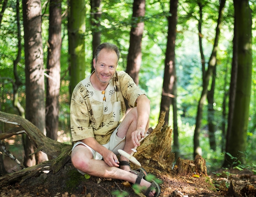 Marc-Andre Selosse siedzi po turecku na leśnej ściółce, trzymając w ręce grzyba.