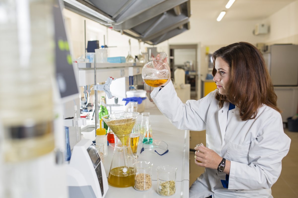 Dr inż. Monika Sterczyńska podczas pracy w labolatorium, trzyma w rękach przezroczyste naczynie z bursztynowym płynem