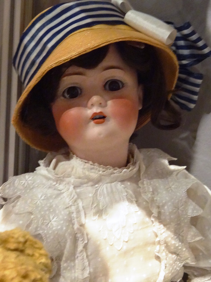 Porcelanowa lalka w białej koronkowej sukience i słomkowym kapeluszu z czarno-białą wstążką. Lalka pochodzi z kolekcji Marka Sosenko, znajdującej się w Muzeum Podkarpackim w Krośnie. Fotografia autorstwa Doroty Żołądź-Strzelczyk.