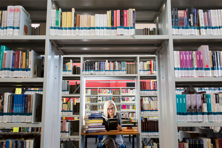 Dr hab. Monika Szczepaniak siedzi w głębi, między regałami bibliotecznymi czytając książkę.