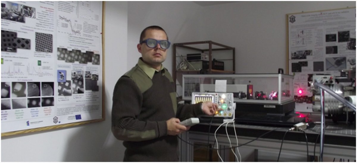 Przemysław Wachulak w okularach ochronnych stoi przy aparaturze badawczej