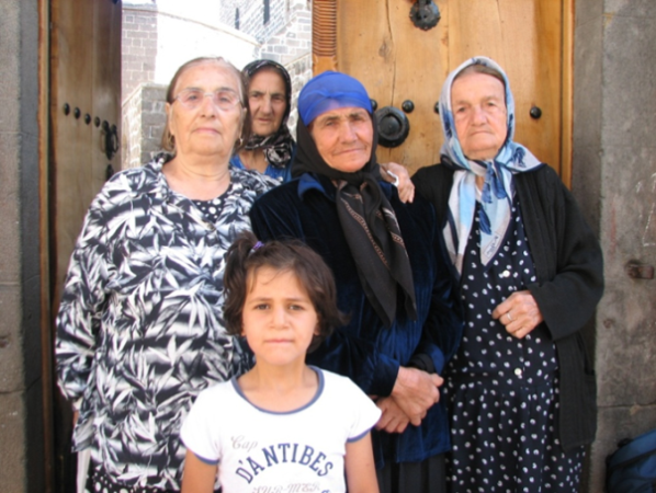 Cztery starsze kobiety i jedna dziewczynka stoją przed otwartymi drewnianymi drzwiami